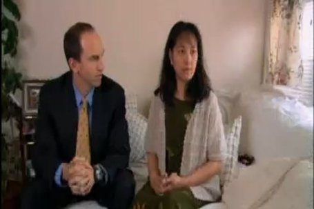 A man in a suit and a woman are seated indoors.