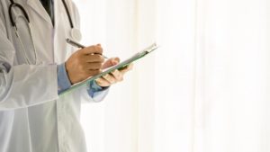 doctor writing on a clipboard by a hospital window